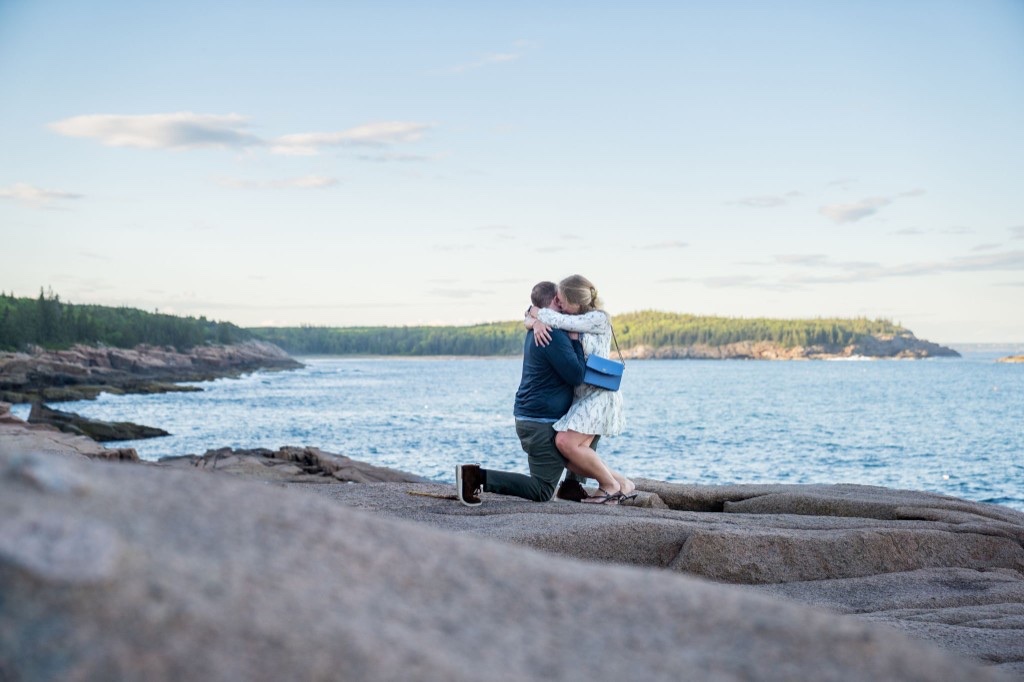 Gregory on one knee proposing to Cecylia on the rocks by the ocean