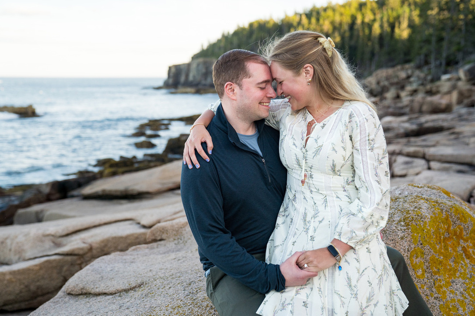 Cecylia and Gregory sitting close together on the rocks with the coastline behind them