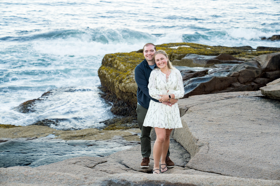 Cecylia and Gregory embracing on the rocks as waves crash behind them